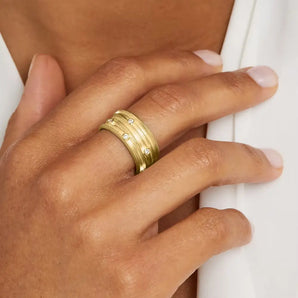 A close-up image of a person's hand wearing a wide gold ring with diamond accents on the finger.