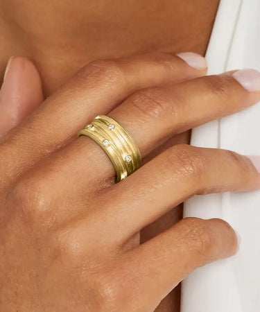 A close-up image of a person's hand wearing a wide gold ring with diamond accents on the finger.