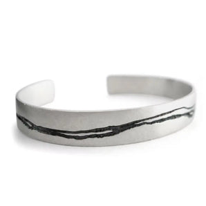 A hand etched silver cuff bracelet with oxidised patterning and a textured finish.