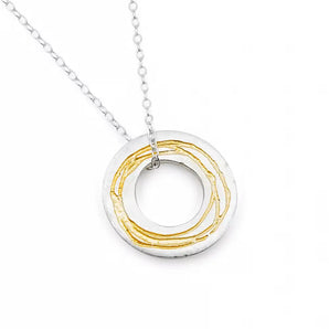 A sterling silver necklace with a gold etched pendant, featuring a hand-drawn pattern in relief, moved freely on a silver trace chain with a bolt ring catch.