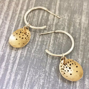 A pair of hoop earrings with gold-colored drops on silver-colored hooks, featuring a pattern of holes arranged in a circular design.