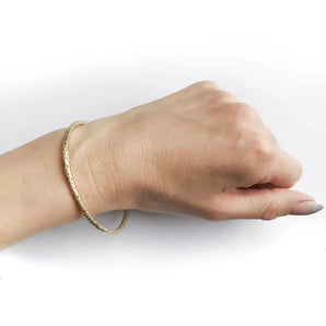 A hand wearing a gold bangle with a halo patterned design.