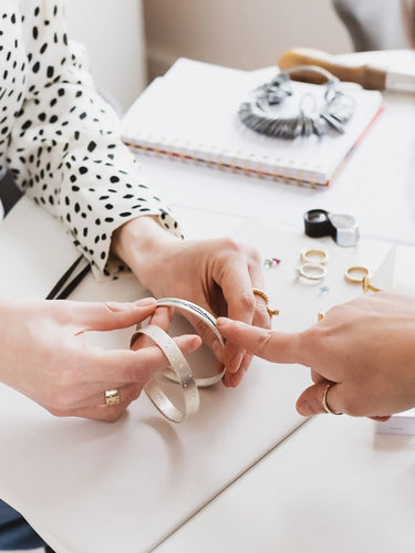 Person trying on a ring with Kate Smith assisting, on a table with jewellery and a notebook.