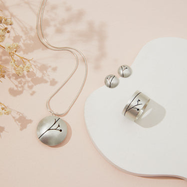 Silver jewelry set with necklace, earrings, and ring on a pink background