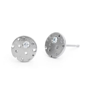 A pair of silver earrings with a frosted texture and central brilliant cut diamond, set in a circular design with burnished edges and a stud fitting.