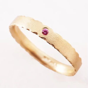 A 9ct yellow gold ring with a brilliant cut pink diamond set on top, featuring a textured and slightly rounded band.