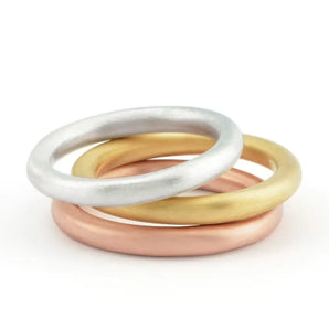 A set of three stackable rings, with the top ring in silver, the middle ring in rose gold, and the bottom ring in yellow gold, all satin finished.