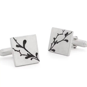 A pair of silver cufflinks with engraved floral details and a satin finish.
