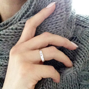 A person's hand wearing a slim silver ring with patterning, resting on a grey knitted surface.