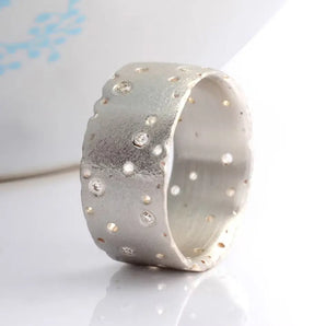 A sterling silver wide band eternity ring with a patterned design and scattered brilliant cut diamonds set against a frosted finish.